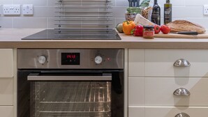 A modern kitchen with a built-in oven, a stainless steel range hood, and a variety of fresh produce on the counter. - Trinity Cottage, YORK (York)