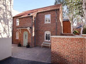 A brick building with a tiled roof, a green door, and a bench in the courtyard.