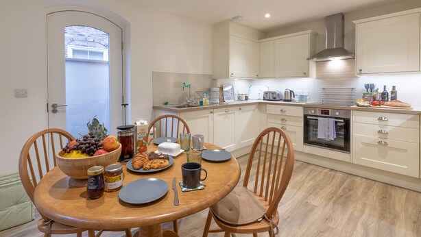 A modern kitchen with white cabinets, a built-in oven, and a dining area with a wooden table and chairs. - Trinity Cottage, YORK (York)