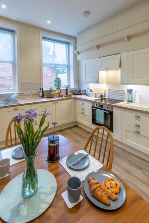 Une cuisine moderne avec des meubles blancs, une table à manger ornée d’un vase de fleurs et une assiette de croissants.