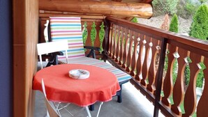 Une terrasse en bois avec une table et des chaises, une rambarde et une vue sur la verdure.