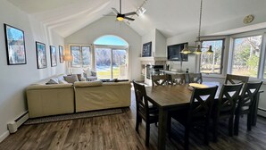 A spacious living area with a high ceiling, a dining table, and a kitchen in the background.