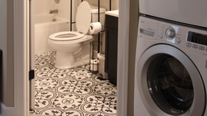 Un cuarto de lavado con lavadora y secadora, un inodoro y un estante con toallas dobladas.