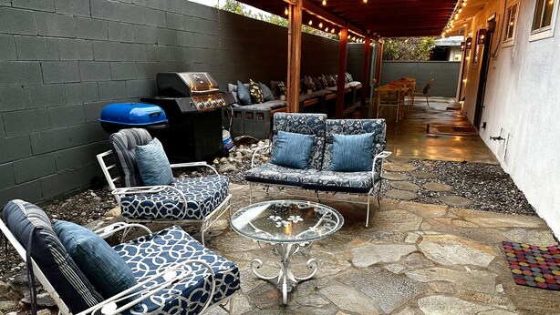 Un patio exterior con suelo de piedra, una parrilla de barbacoa y disposición de asientos que incluye sofás y sillones estampados.