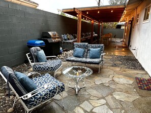 Une terrasse extérieure dotée d’un sol en pierre, d’un barbecue et d’un mobilier comprenant des canapés et des fauteuils aux motifs variés.