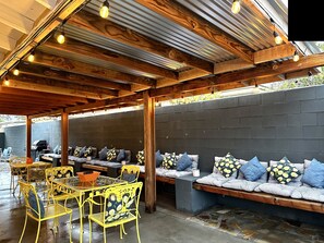 An outdoor patio with wooden beams, a seating area with patterned cushions, and a table with chairs. - Casa Sunny Dunes: a Private, Mid-Century Oasis (Palm Springs)