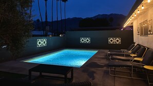 Piscina exterior con sillones de descanso y una mesa, rodeada por un muro bajo con diseños geométricos.