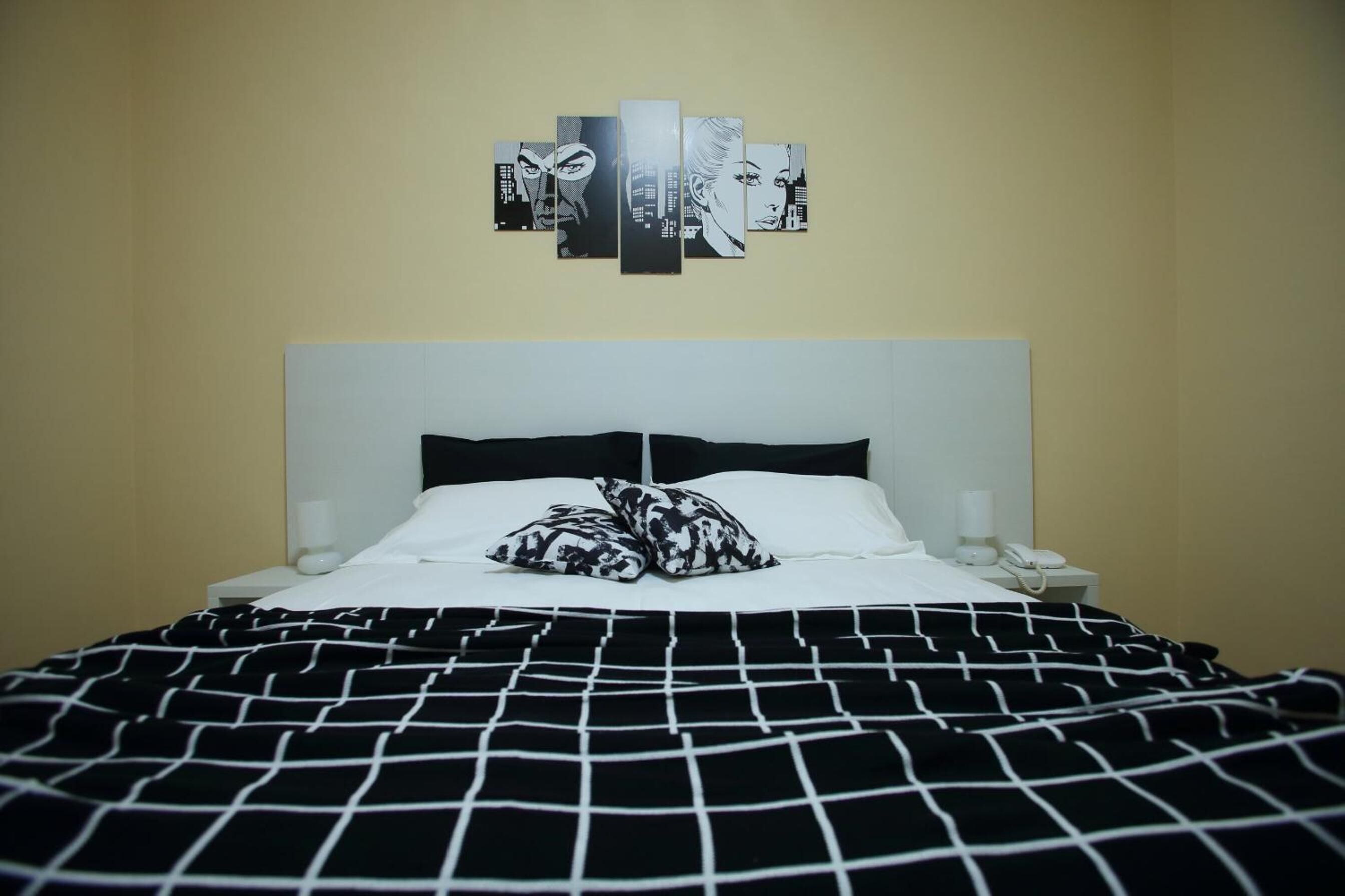 A bed with a black and white checkered bedspread, two black and white patterned pillows, a white headboard, and a wall-mounted artwork above the bed.