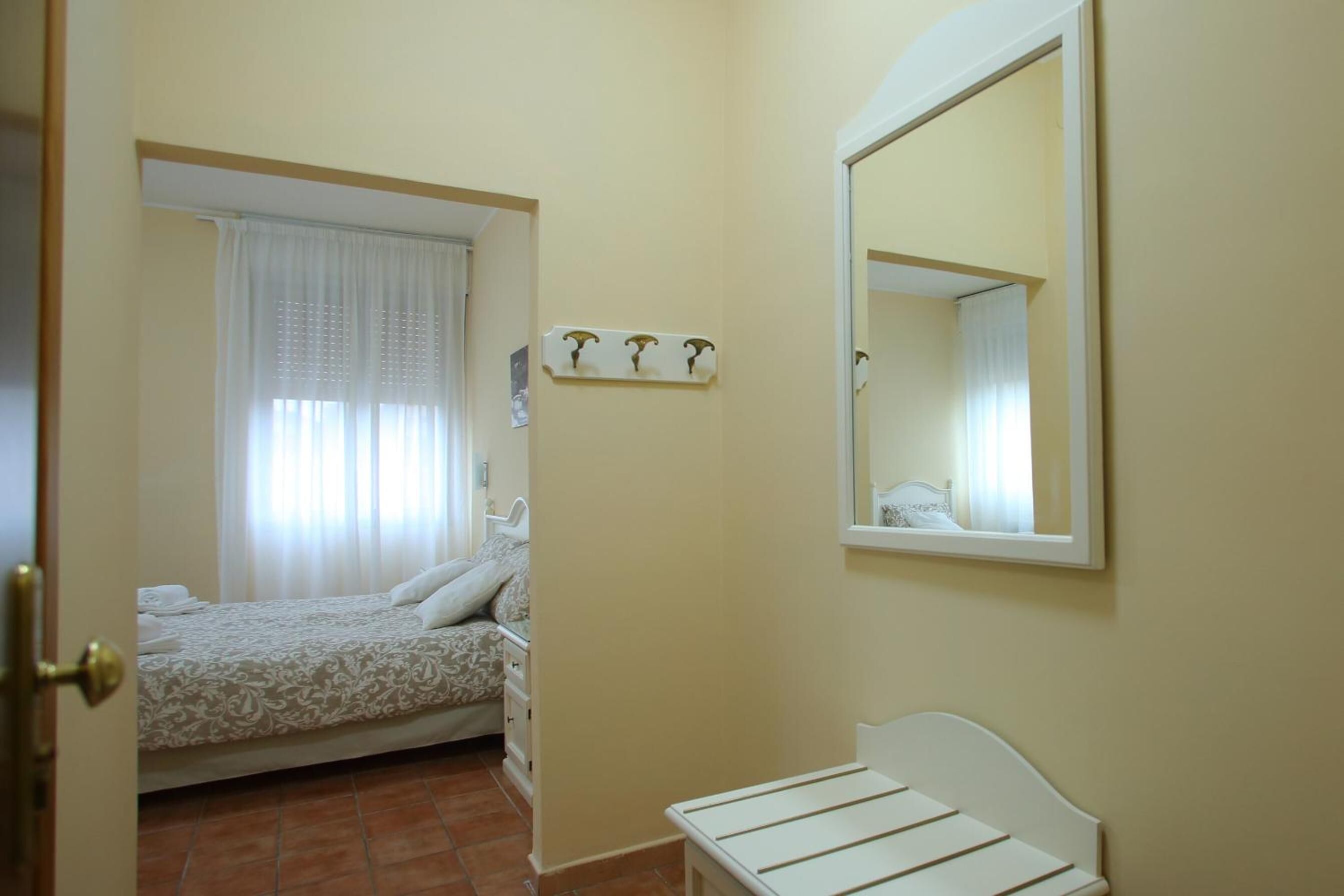 Ein Schlafzimmer mit einem Bett, einem kleinen Tisch, einem Spiegel und einem Fenster mit Vorhängen.