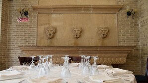 A dining area with a brick wall, a fireplace with three carved faces, and tables set with wine glasses and plates. - Hotel Villa Romana (Piazza Armerina)