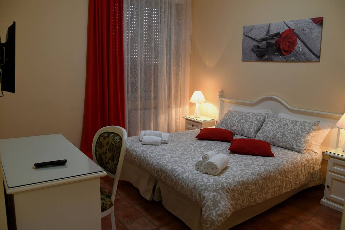 Une chambre bien rangée, avec un lit, des tables de chevet, une chaise, un bureau et un tableau accroché au mur.