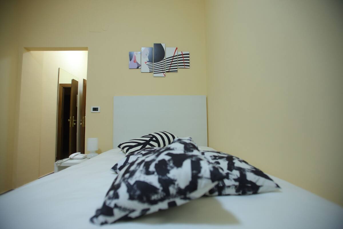 Une chambre d’hôtel comprenant un lit, une table de chevet avec une lampe, un téléphone et une œuvre d’art accrochée au mur.