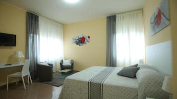 A hotel room with a bed, a desk, a chair, a TV, and a painting on the wall.
