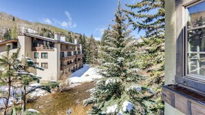 A multi-story building with balconies, a snow-covered landscape, and a river. - 1-#28 One Willow Bridge 3BD (Vail)