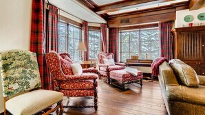 A traditional room with wooden floors, large windows, and classic furniture including a red upholstered sofa, a floral armchair, and a leather armchair. - 1-#28 One Willow Bridge 3BD (Vail)