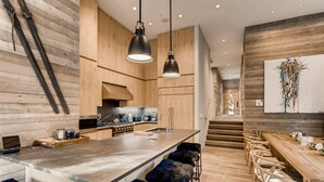 A modern kitchen with wooden cabinetry, a central island with bar stools, and a staircase leading to an upper level. - 1-184 West Meadow Drive (Vail)