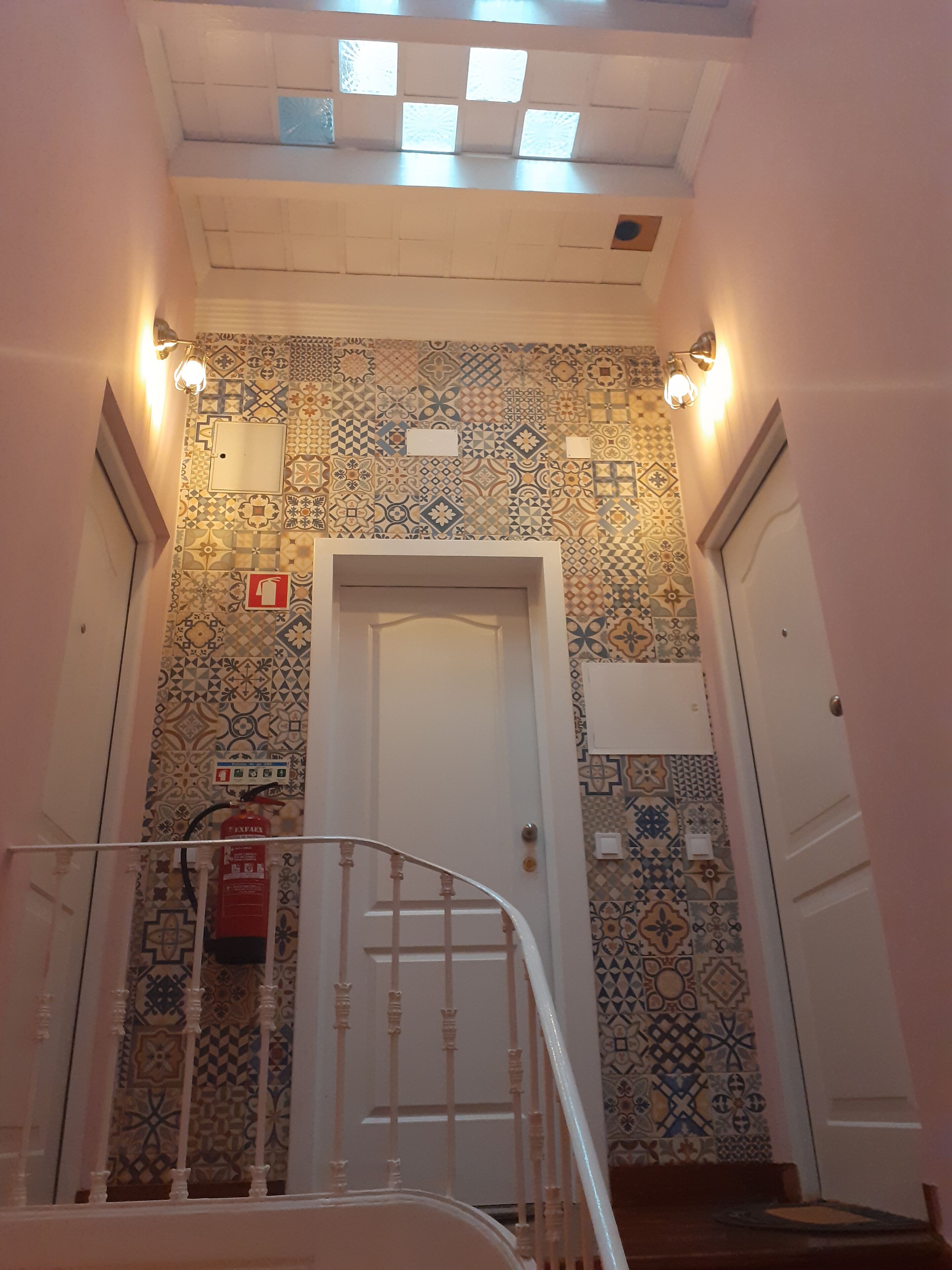Una escalera con barandilla que lleva a una puerta, rodeada de baldosas con diseño.