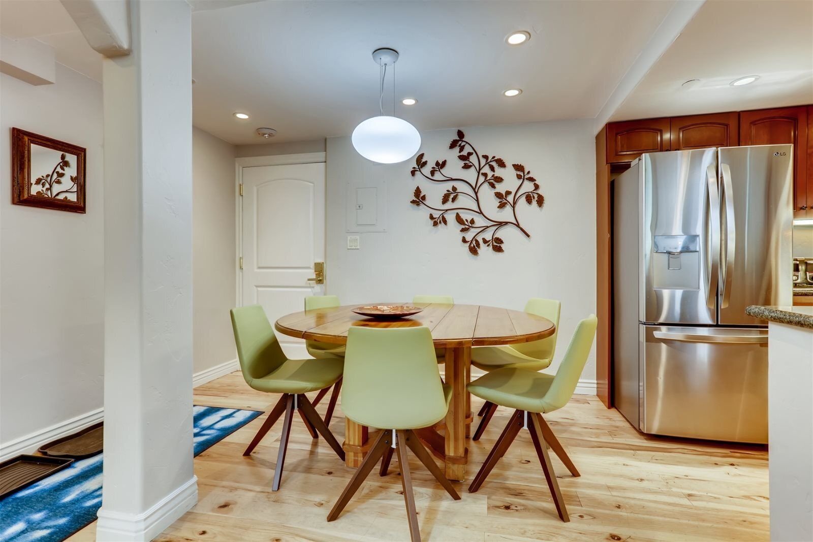 A modern kitchen with a stainless steel refrigerator, wooden dining table, and green chairs.