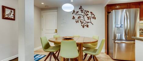 A modern kitchen with a stainless steel refrigerator, wooden dining table, and green chairs.