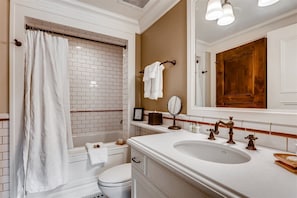 Bagno con vasca da bagno bianca, un water, un lavandino con un ampio specchio e una porta in legno.