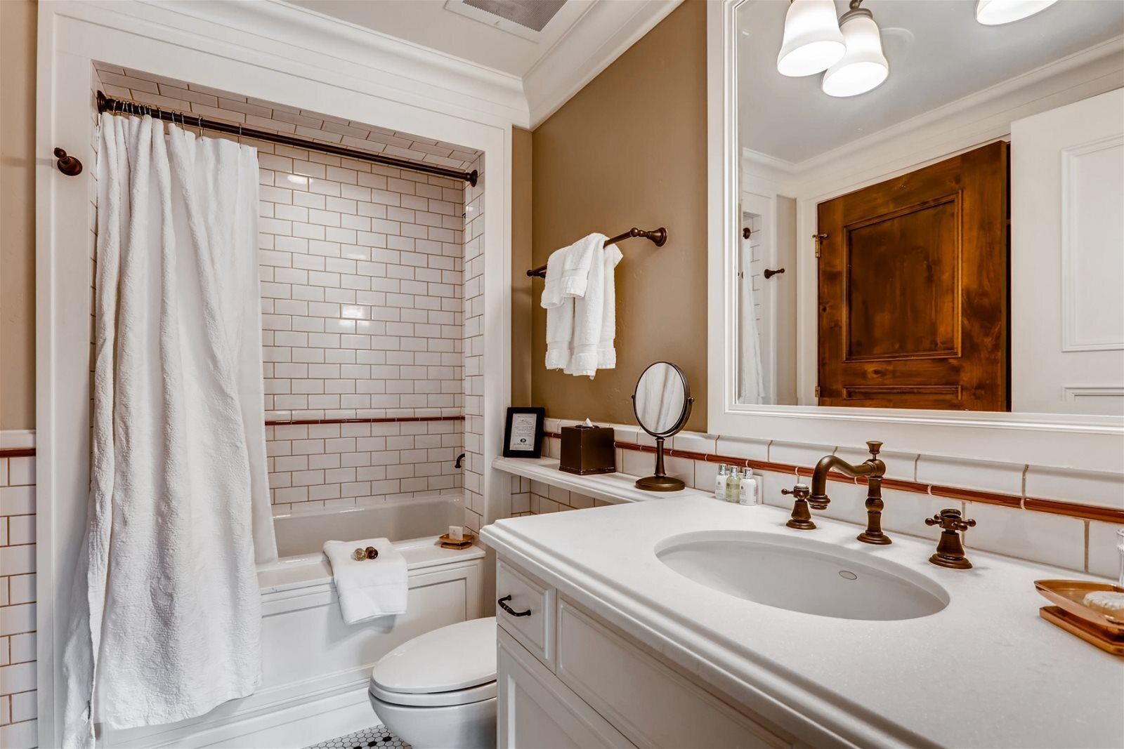 Un baño con una bañera blanca, un inodoro, un lavabo con un espejo grande y una puerta de madera.