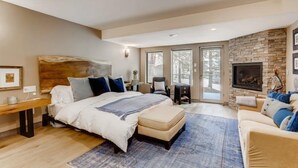A spacious bedroom with a large bed, a stone fireplace, and a view through the glass doors.