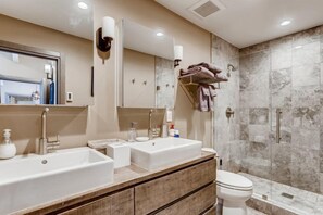 A modern bathroom with two sinks, a toilet, a glass shower enclosure, and a towel rack with folded towels. - 1-970 Fairway Ct (Vail)