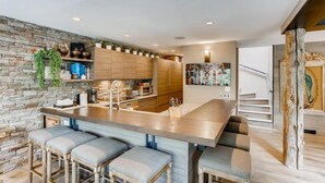 A modern kitchen with a central island, bar stools, and a stone accent wall.