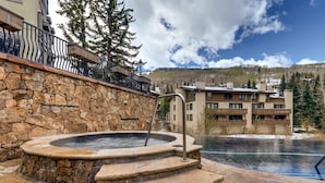 A stone wall with a hot tub, steps leading to a pool, and a building with balconies in the background. - Vail VLG One Willow 3bd-win1 (Vail)