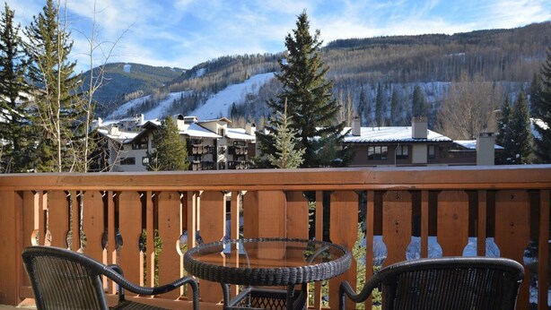A wooden deck with wicker chairs and a glass table, overlooking a snowy mountain landscape with buildings in the background. - Vail VLG One Willow 2bd-joh1 (Vail)