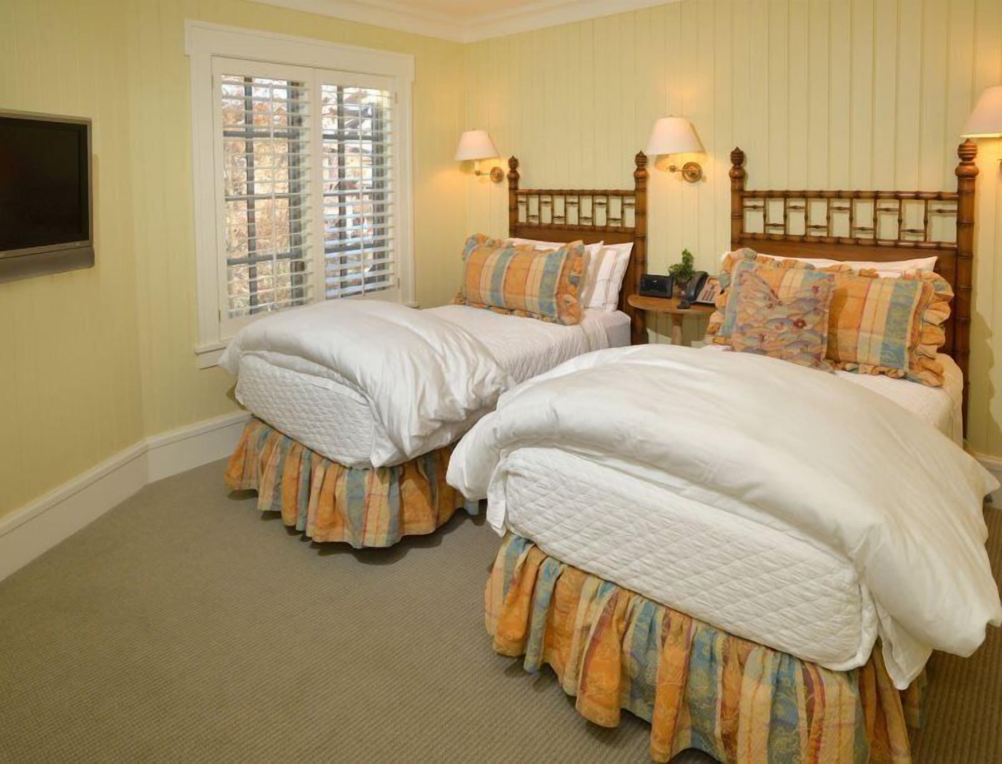 A hotel room with two beds, a television, and a window with blinds.