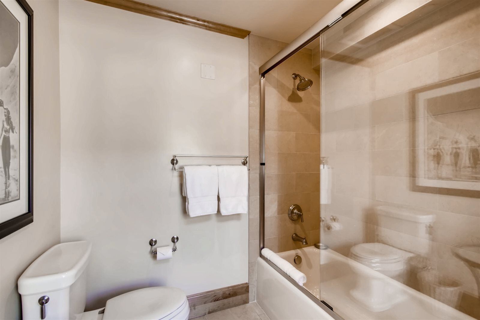 A bathroom with a toilet, a shower, and a bathtub. There are towels hanging on a rack.
