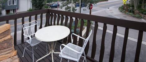 Una terraza de madera con una mesa redonda y dos sillas, con vistas a una calle con coches y una señal de parada.