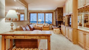 Ein gemütliches Wohnzimmer mit Holztisch, Ledersofa und Kamin aus Stein.
