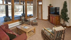 Ein gemütliches Wohnzimmer mit Kamin, Holzmöbeln und großen Fenstern mit Blick auf eine verschneite Landschaft.