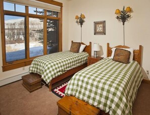 A bedroom with two single beds, a window with a view of a snowy landscape, and a small wooden chest. - 1-arrowhead 45 River Dance Way 5 bed (Edwards)
