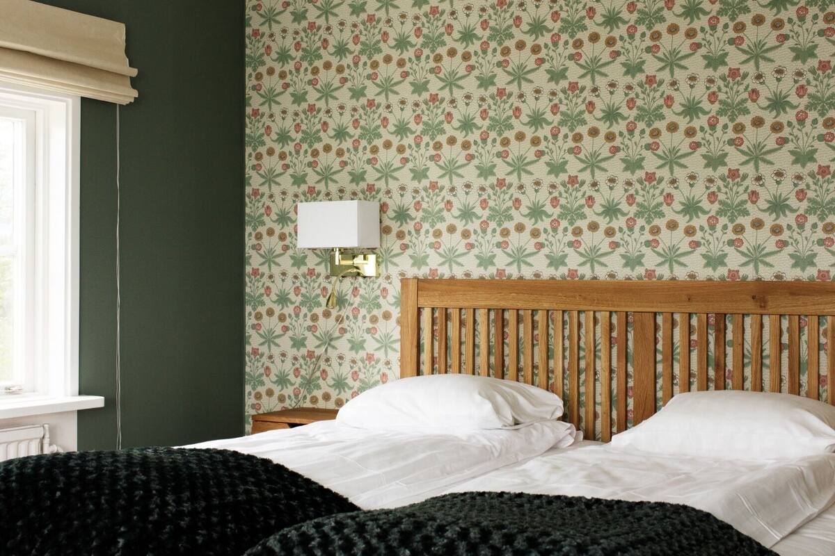 A bedroom with a wooden headboard, two white beds, a green wall, and a floral patterned wallpaper.