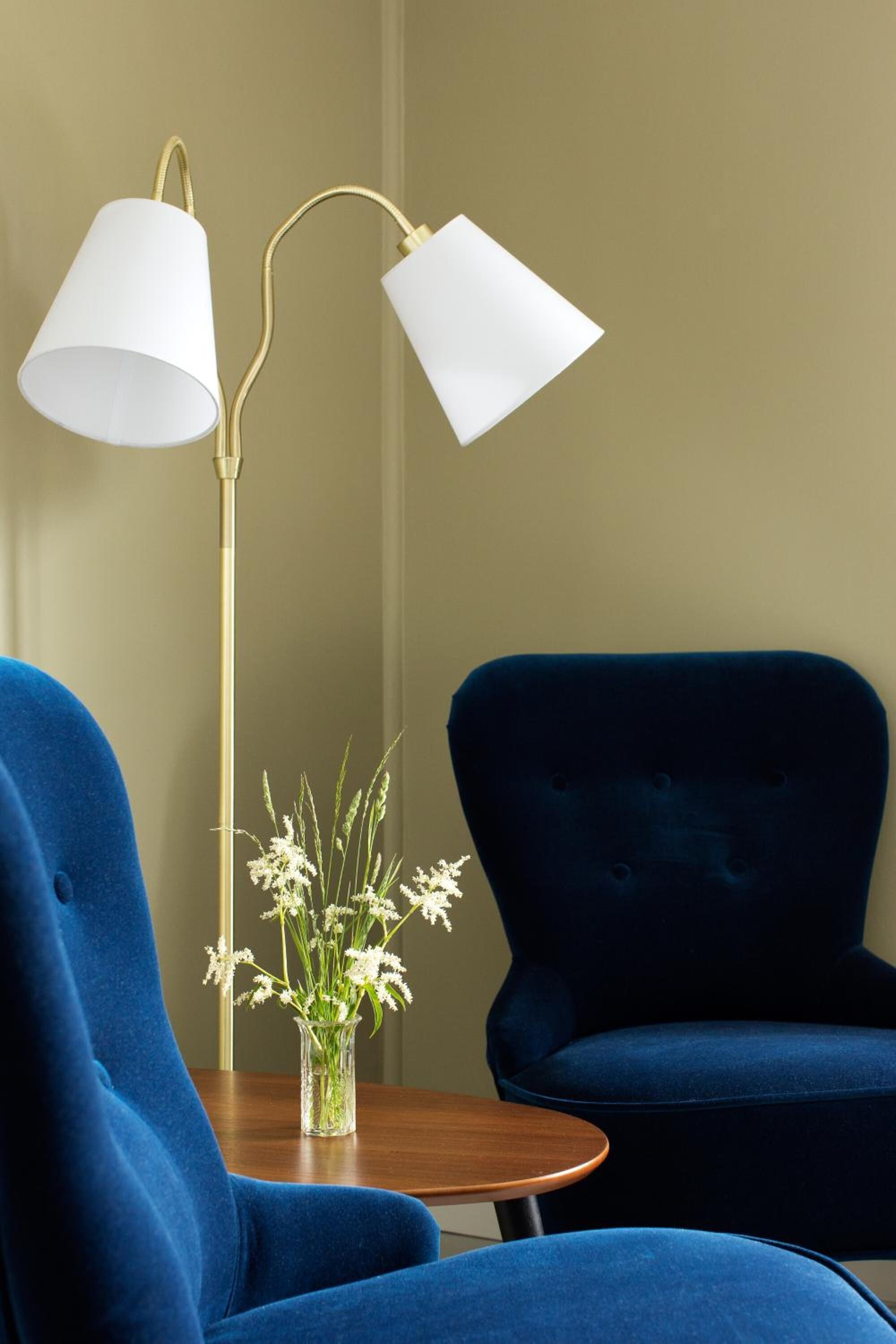 Una habitación con un sillón azul, una mesa redonda de madera y una lámpara de pie con pantallas blancas.