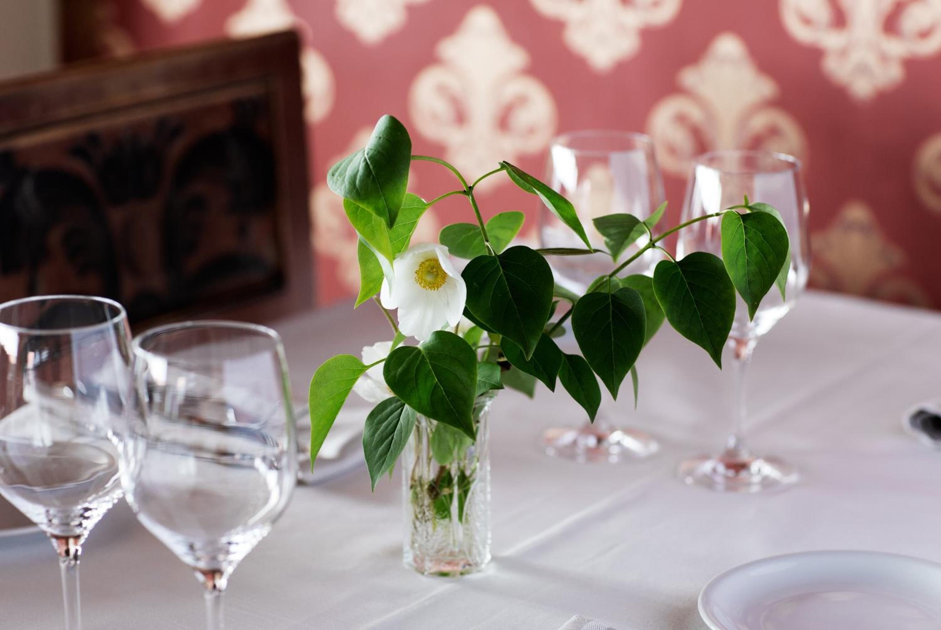 A table set with clear glassware and a vase with a white flower and green leaves.