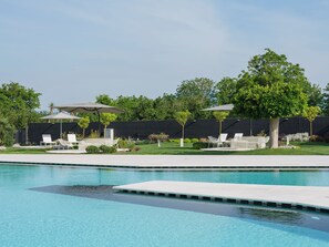 A swimming pool with a clear blue water surface, surrounded by a grassy area with white lounge chairs and umbrellas. - Secret Garden (Palma Campania)