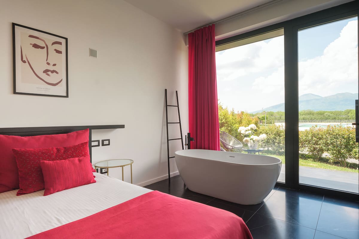 A modern bedroom with a large bed, a bathtub, and a view of a lake and mountains.