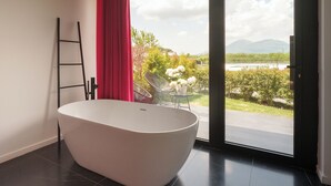 A modern bathroom with a freestanding bathtub, a glass table with flowers, and a view of a garden and mountains through a large sliding door. - Secret Garden (Palma Campania)