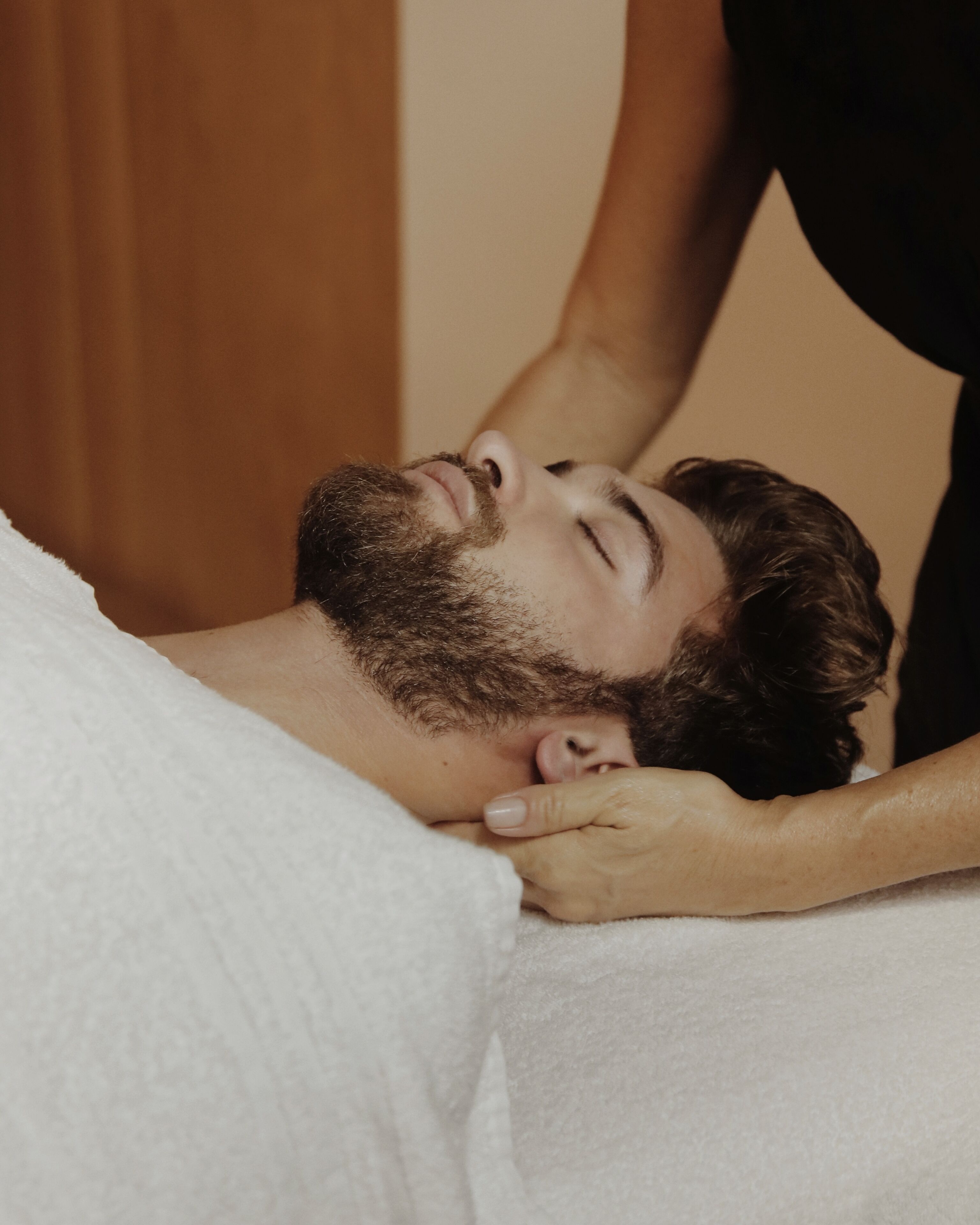 A person lying on a bed with a white blanket, receiving a massage.