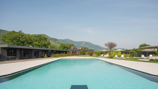 A swimming pool with a modern design, surrounded by a landscaped garden and a building with large windows. - Secret Garden (Palma Campania)