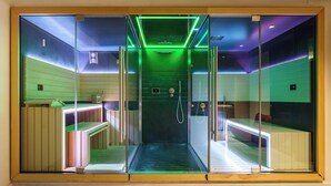 A modern spa room with a glass partition, wooden benches, and green ambient lighting. - Secret Garden (Palma Campania)