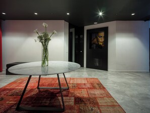 A modern lobby with a round table, a vase with flowers, a red patterned rug, and a large poster on the wall. - Secret Garden (Palma Campania)