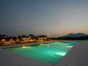 A swimming pool with a view of mountains in the background, surrounded by lounge chairs and a covered area with lights. - Secret Garden (Palma Campania)