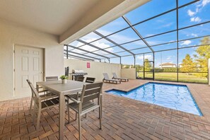 A covered outdoor area with a pool, a table with chairs, and a grill. - Theme Rooms! 5BR Townhouse w Pool in Kissimmee (Kissimmee)