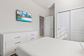 Une chambre à coucher avec un lit, un téléviseur fixé au mur et une armoire blanche.