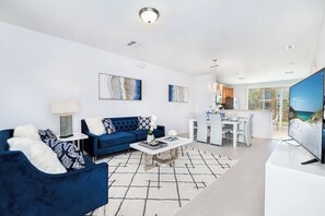 Un salon moderne avec un canapé bleu, une table basse blanche et un téléviseur à écran plat.
